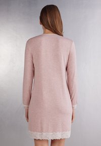 Ljusrosa nattklänning med långa ärmar, tillverkad av mjukt tyg, med en spetskant längs fållen och ärmarna, slät textur, knälång.