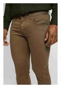 Bruine denim broek met een slim fit, zichtbare zakken en een gladde textuur. Gestyled met een knop- en ritssluiting.