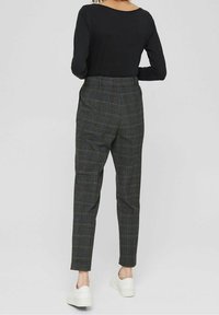 Zwart top met lange mouwen gecombineerd met geruite broek in grijs, blauw en groen, met taps toelopende pijpen en zijzakken, gedragen met witte sneakers.