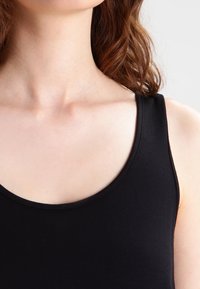 Débardeur noir avec un décolleté arrondi et de larges bretelles, fabriqué dans un tissu lisse et léger. Vue en gros plan mettant en avant la zone du col.