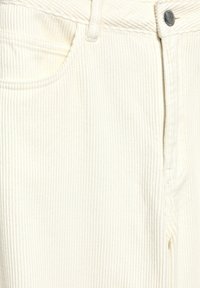 Zbliżenie na białe spodnie z sztruksu ukazujące pionową prążkowaną fakturę, przednią kieszeń, szlufkę na pasek i srebrne zapięcie na guzik.