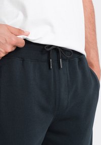 Pantalons de survêtement bleu marine foncé avec taille élastique à cordon de serrage, ceinture côtelée et poches latérales. Le tissu semble doux et a une texture lisse.