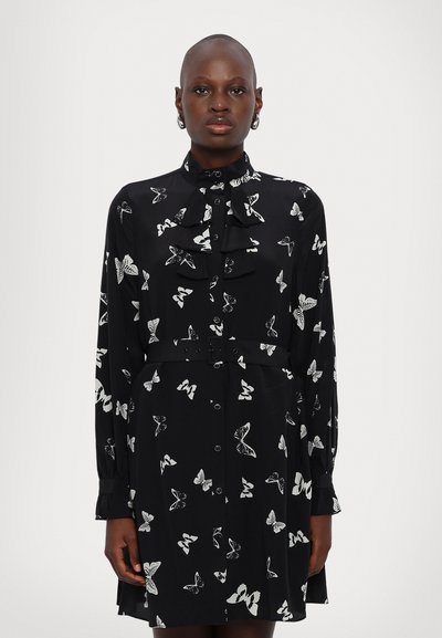 Robe noire avec un motif de papillon blanc, dotée de manches longues, d'un col à volants, d'une fermeture à boutons et d'un détail de taille à nouer.