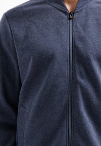 Marineblauwe ritsjack gemaakt van textuurstof met een opstaande kraag en zijzakken. Beschikt over een soepele rits en een casual pasvorm.