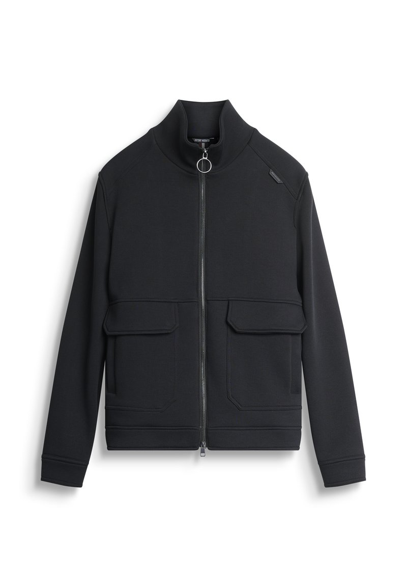 Chaqueta negra con cuello alto, cremallera frontal y dos grandes bolsillos de parche. Textura suave con costuras en contraste y acento metálico.