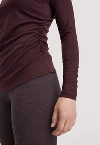 Dunkelburgunderrotes Langarmshirt mit gerafften Seitendetails, kombiniert mit dunkelgrauen leggings mit gebogenen Nahtakzenten. Weicher Stoff.