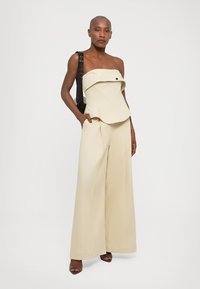 Top peplum sem alças em bege com detalhe de botões frontais, combinado com calças largas numa tonalidade similar e uma mala de ombro texturizada em preto.