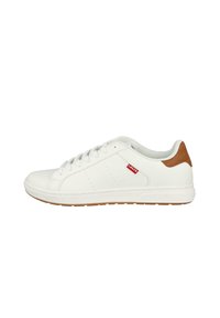 Zapatilla blanca con un upper de cuero suave, acento en el talón en color marrón y detalles de perforación mínimos. Presenta una suela de goma y cordones. Etiqueta de logotipo rojo.
