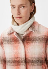 Płaszcz w kratę z mieszanki wełny w odcieniach różu, pomarańczy i brązu. Posiada prążkowany biały kołnierz oraz fakturowany materiał o miękkim wykończeniu.