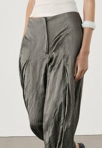 Luźne spodnie w ciemnoszarym kolorze. Mają wysoką talię, miękką teksturę oraz zwiewny krój z bocznymi fałdami.