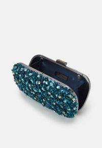 Liten rektangulär clutch öppen, dekorerad med teal-färgade pärlor och paljetter, silverram och marinblå inredning.