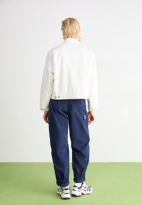 Vitt jeansjacka med krage, kombinerad med marinblå cargobyxor med fickor. Modellen har på sig vita och röda sportskor. Grön golv.