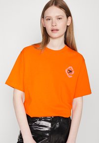 Heldoranje T-shirt van katoen, met een ronde hals en korte mouwen. Bevat een cirkelvormige grafiek op de linker borstkas.