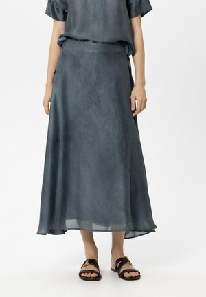 Person trägt einen dunkelgrauen Midirock mit feiner Struktur, kombiniert mit einem passenden Oberteil und schwarzen flachen Sandalen mit goldenen Schnallen.