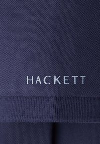 Granatowy materiał z teksturowanym splotem. Nazwa marki "HACKETT" jest nadrukowana na srebrno, umiejscowiona blisko dolnej krawędzi.