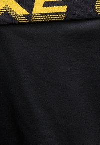 Μαύρο ύφασμα με πτυχή που δείχνει μια μαύρη και κίτρινη υφαντή ετικέτα ή ταινία κατά μήκος της πάνω άκρης.