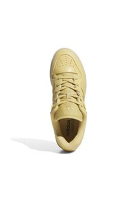 Zapatilla amarilla de Adidas con cordones, puntera perforada y logo en la lengüeta, mostrada desde una vista superior con sombra sobre fondo blanco.