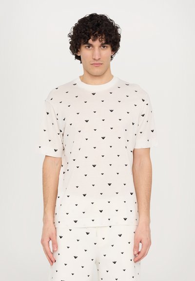 Camiseta de manga corta color crema con patrón en forma de corazón negro, corte relajado, tejido suave, escote redondo, combinada con pantalones a juego.
