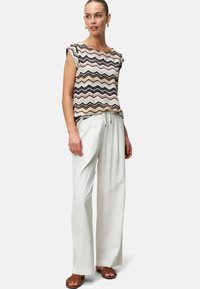 Patterned knit top with short sleeves, featuring zigzag design in beige, black, and brown; paired with white wide-leg trousers and brown sandals.