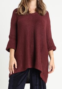 Burgundy stickad tröja med lös passform, trekvartsärmar, texturerat mönster och V-hals, kombinerad med marinblå manchesterbyxor.