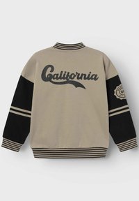 Sweatshirt beige avec des manches noires, un col côtelé et des poignets rayés. Présente un grand texte "California" et un design de badge sur la manche gauche.