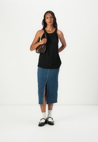 Svart ermeløs topp med rynket halslinning, blå denim blyantskjørt med frontsplitt, svarte slip-on sko og brun skulderveske.