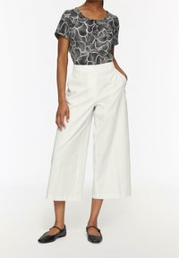 Top corto a maniche corte a motivi bianco e nero abbinato a pantaloni bianchi a gamba larga. La modella indossa scarpe flat nere. Design semplice e moderno.