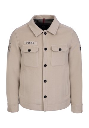 Beige knöpfbare Jacke mit zwei Brustklappentaschen, Seitentaschen, schwarzen Knöpfen und einem "II-UK REG." Aufnäher auf der rechten Brust.