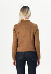 Veste en daim marron avec une coupe ajustée, un col montant et des détails de couture. Portée sur un jean en denim foncé. Vue de dos présentée.