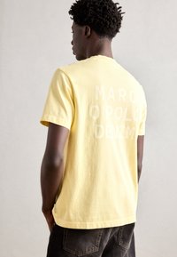 Yellow cotton t-shirt with short sleeves, featuring white block text "MARC O'POLO DENIM" on the back. Casual fit with round neckline.