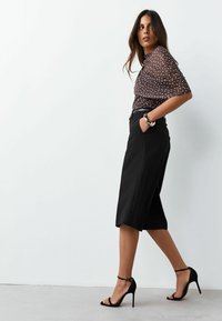 Brown polka dot sheer blouse, black tailored culottes, and black strappy high-heeled sandals. Model posing against a plain background.