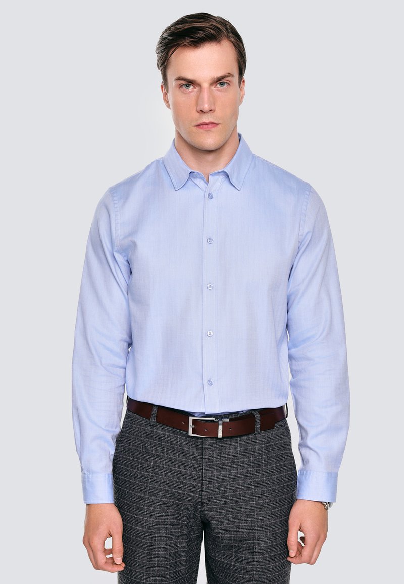Jasnoniebieska koszula z długim rękawem i guzikiem, z klasycznym kołnierzykiem, gładką teksturą i subtelnym połyskiem; zestawiona z szarymi spodniami w kratę i brązowym paskiem.