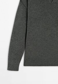 Manche et partie du torse d'un pull en tricot gris foncé avec poignets et ourlet côtelés sur fond blanc.