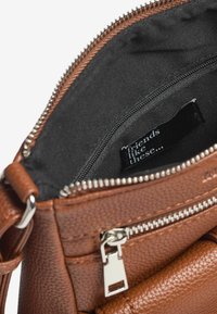 Borsa a tracolla in pelle marrone con zip argentate, che mostra un interno in tessuto nero con un'etichetta che recita "amici come questi..."