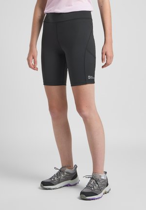 Pantaloni sportivi neri con vita alta, texture liscia e cuciture a contrasto, abbinati a scarpe da trail grigie con accenti viola.