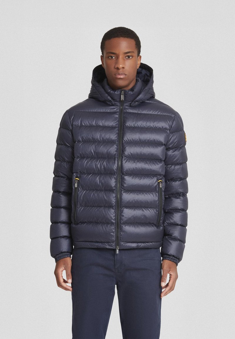 Giubbotto imbottito blu navy con cappuccio, caratterizzato da un design trapuntato, chiusura frontale con zip e tasche laterali con zip. Texture liscia e forma imbottita.