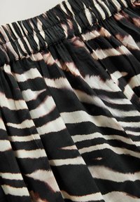 Zwart-witte stof met een zebra-stripe patroon, voorzien van een geplooide elastische tailleband en een zacht, textuur materiaal.