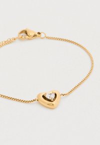 Χρυσό βραχιόλι με μενταγιόν σε σχήμα καρδιάς που έχει ένα διαφανές, πολύγωνο πολύτιμο λίθο στο κέντρο· κομψός σχεδιασμός αλυσίδας με κούμπωμα ψαροκόκκαλο.