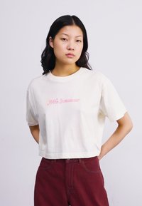 Vit kortärmad t-shirt i mjuk bomull med rosa kursiv text som säger "Nike Sportswear." Korta ärmar och avslappnad passform.