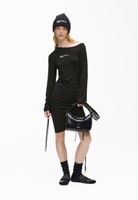 Μαύρο φόρεμα με μακριά μανίκια, στενή γραμμή και πτυχώσεις, συνδυασμένο με μαύρο πλεκτό σκουφί και γυαλιστερή μαύρη τσάντα, φορεμένο με ψηλές κάλτσες και παπούτσια.