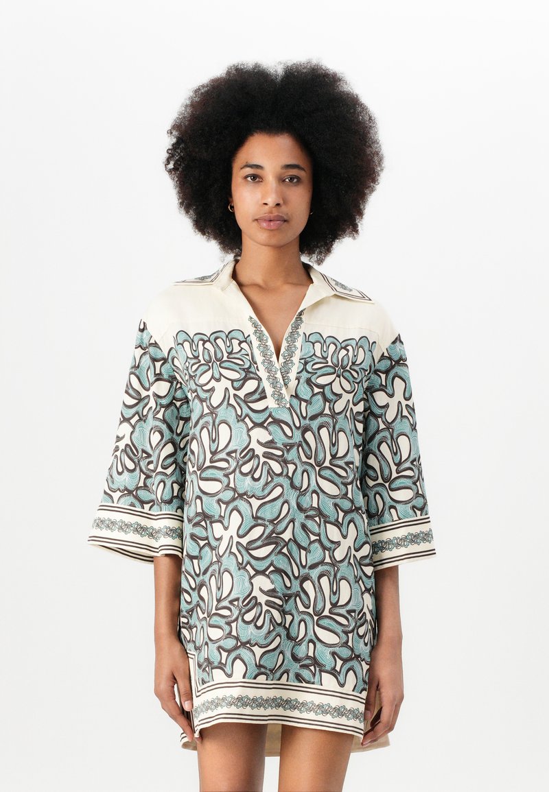 Tunic cu mânecă scurtă de culoare crem, cu un model floral albastru și maroniu, guler și detalii decorative pe mâneci și tiv.