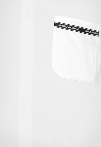 Vit kortärmad skjorta med en bröstficka som har ett svart Emporio Armani-logoband och knäppning fram.