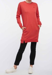Rotes Sweatshirtkleid mit langen Ärmeln, seitlichen Taschen und gespaltenem Saum, getragen mit schwarzen Leggings und weißen Sneakers. Weicher Stoff.