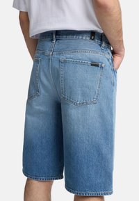 Shorts en denim bleu clair, avec une finition légèrement délavée. Comprend deux poches arrière et une étiquette sur la taille. Ourlés au niveau du genou.