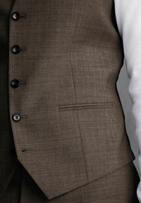 Gilet de costume marron texturé avec six boutons noirs, poche poitrine unique et une coupe soignée, associé à une chemise blanche.