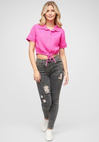 Rosa, kortermet, kragecrop topp med knapp foran og snøring, kombinert med mørkegrå ripped skinny jeans og hvite sneakers.