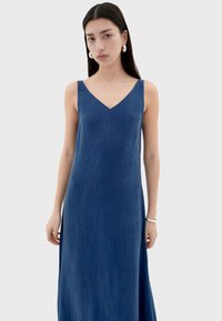 Blauwe maxi-jurk met een V-hals en dunne bandjes. Gemaakt van een gladde stof, met een rechte silhouet en zijsplitten.