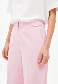 Roze wijde broek van lichtgewicht materiaal. Heeft een gladde textuur, zijzakken en een label op de tailleband.
