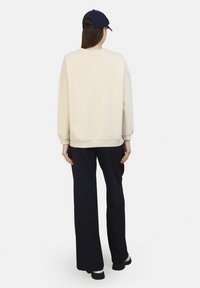Sudadera crema con hombros caídos, puños y dobladillo acanalados, combinada con pantalones de pierna ancha azul marino y zapatos de plataforma negros, vista desde atrás.