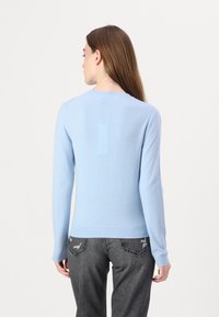 Lys blå strikket genser med lange ermer og rund hals. Har en jevn tekstur og ribbede kanter. Bakvinkel vist.